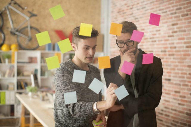 Two colleagues have a post it meeting on glass wall