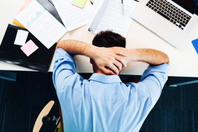men laying on his desk with his hands behind his head with a lot of work on his desk