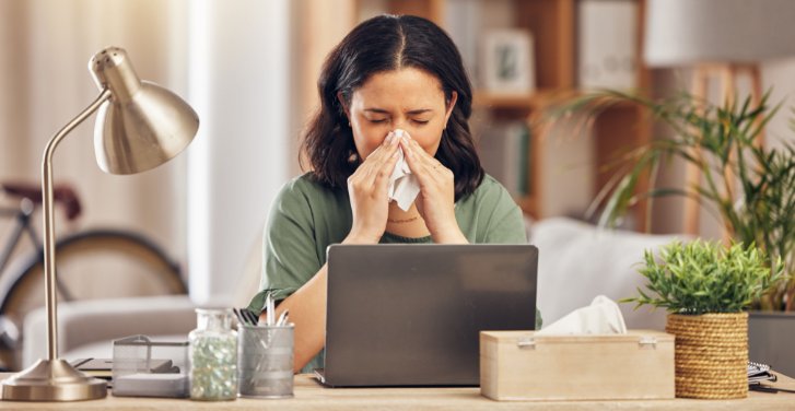 woman blowing her nose while working on her laptop
