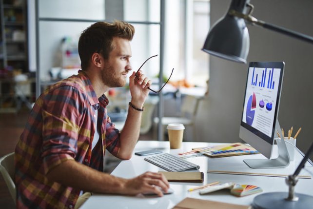 A men analysing graphs on his computer while holding his glasses